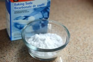 A blue box of baking soda and a glass bowl containing baking soda