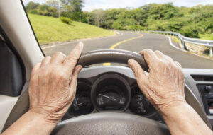 Hands on steering wheel of car with winding road in foreground
