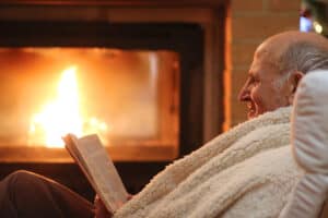 Older man sitting beside fireplace reading a book