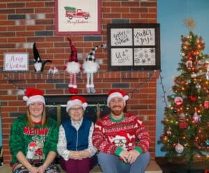 Two women and one man dressed in Christmas outfits.