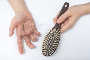Hands holding clump of hair and hairbrush