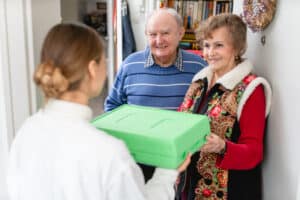 Woman delivering Meals on Wheels meal to elderly couple