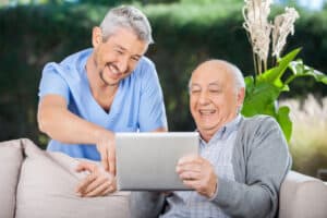 Male nurse and senior man laughing while using digital tablet.