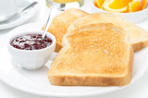Two slices of toast on white plate with little bowl of purple jelly.