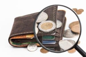 Brown wallet containing credit cards surrounded by a variety of coins.