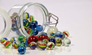 Multi-colored toy marbles spilling out of a glass jar.