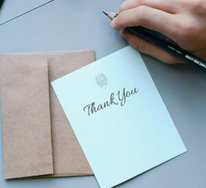 Image of hand holding pen next to than-you note and envelope.