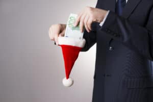 Man wearing a black suit putting money into a red Santa hat.