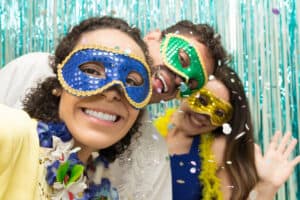 Two women and one man wearing Mardi Gras masks.